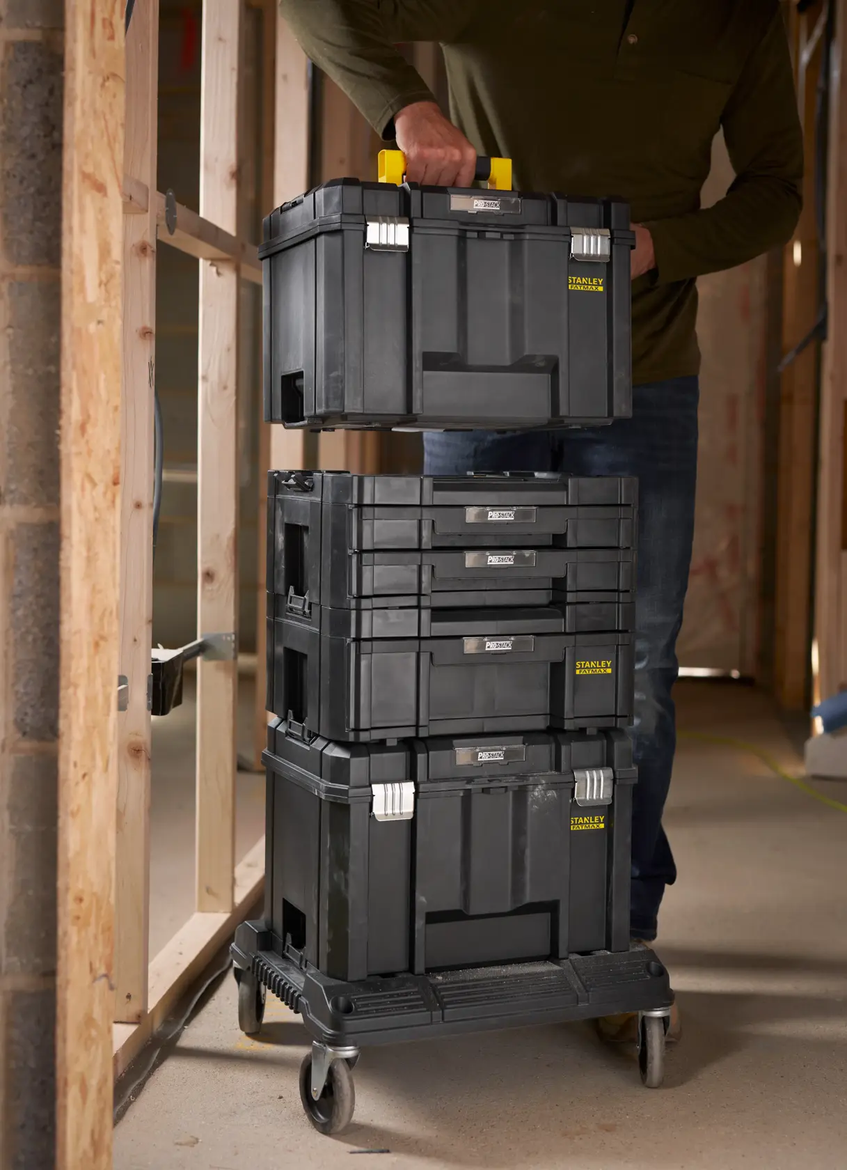 STANLEY FMST1-71972 stackable black toolboxes on rolling cart in workshop, person lifting top box.