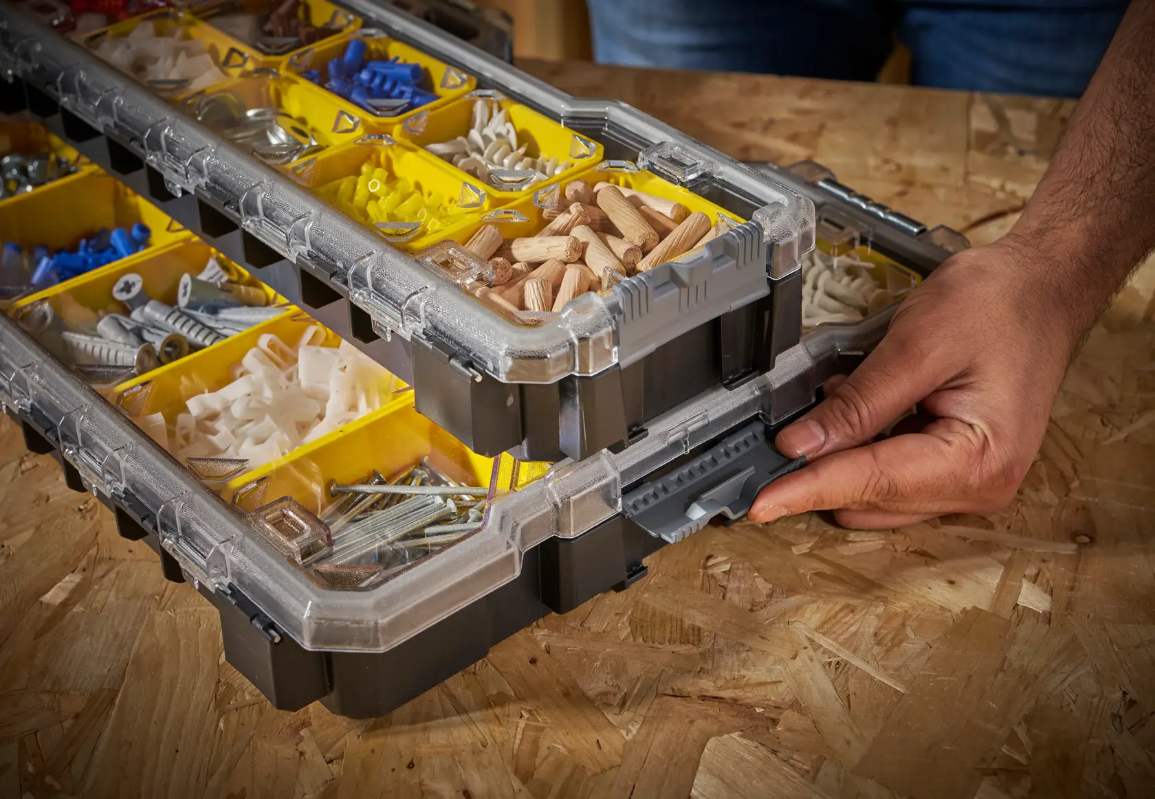 STANLEY FMST1-75781 organizer box with yellow compartments, filled with various hardware, shown on a workbench, hand opening latch.