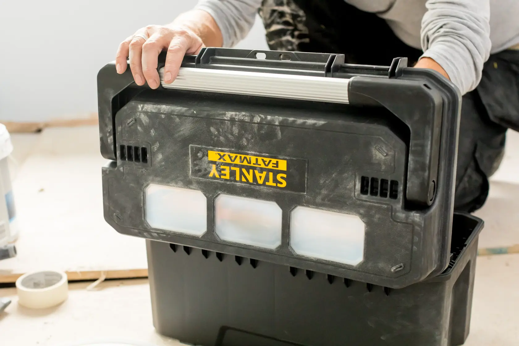 Photo of STANLEY FMST1-75792 black toolbox with transparent compartments being handled in a workspace.