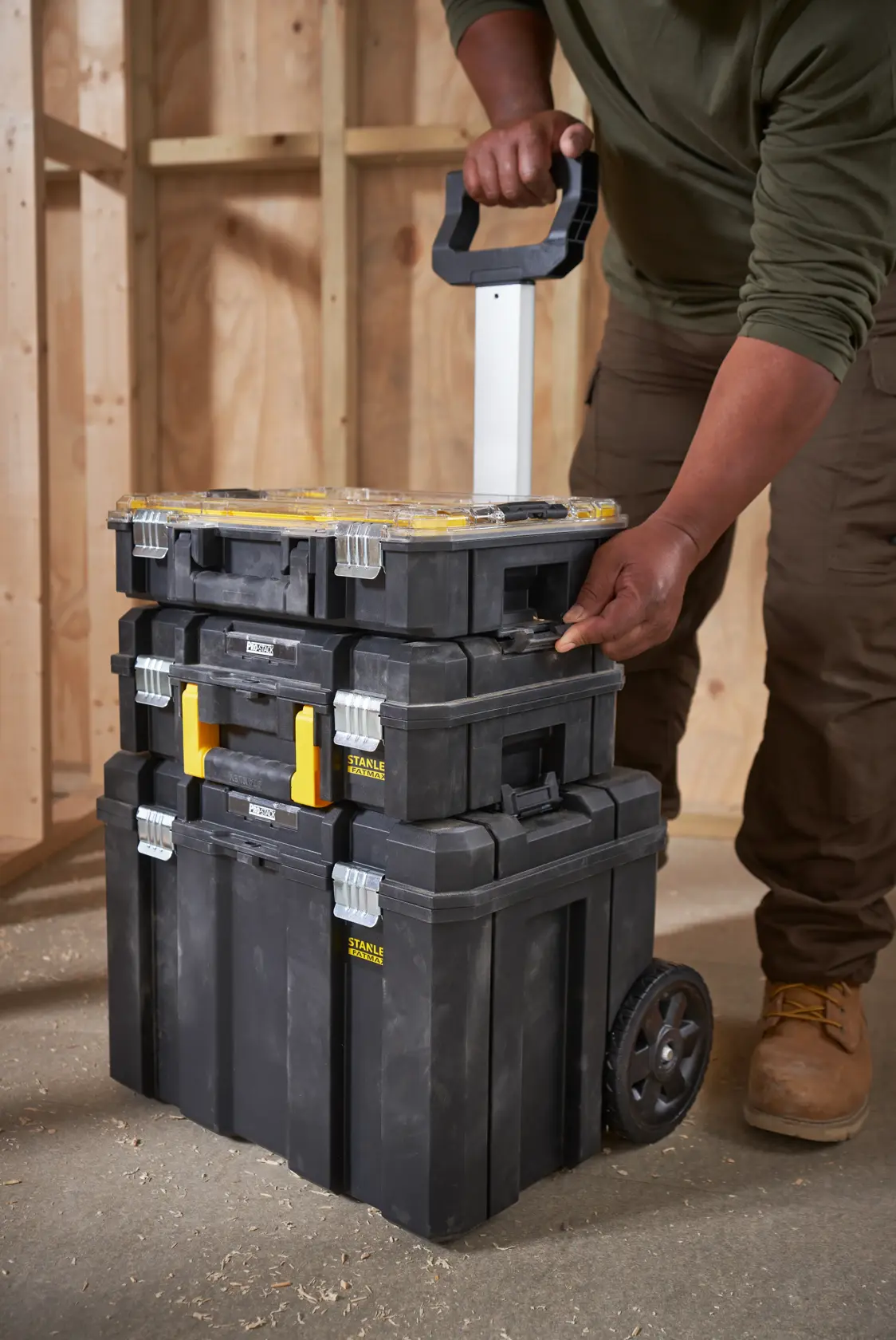 STANLEY FMST1-80101 rolling toolbox stack with three black modular cases, shown being pulled by handle in workshop.