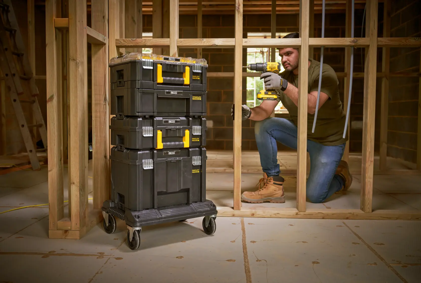 STANLEY FMST1-80107 black stackable toolboxes with yellow handles on wheeled base in a construction site.