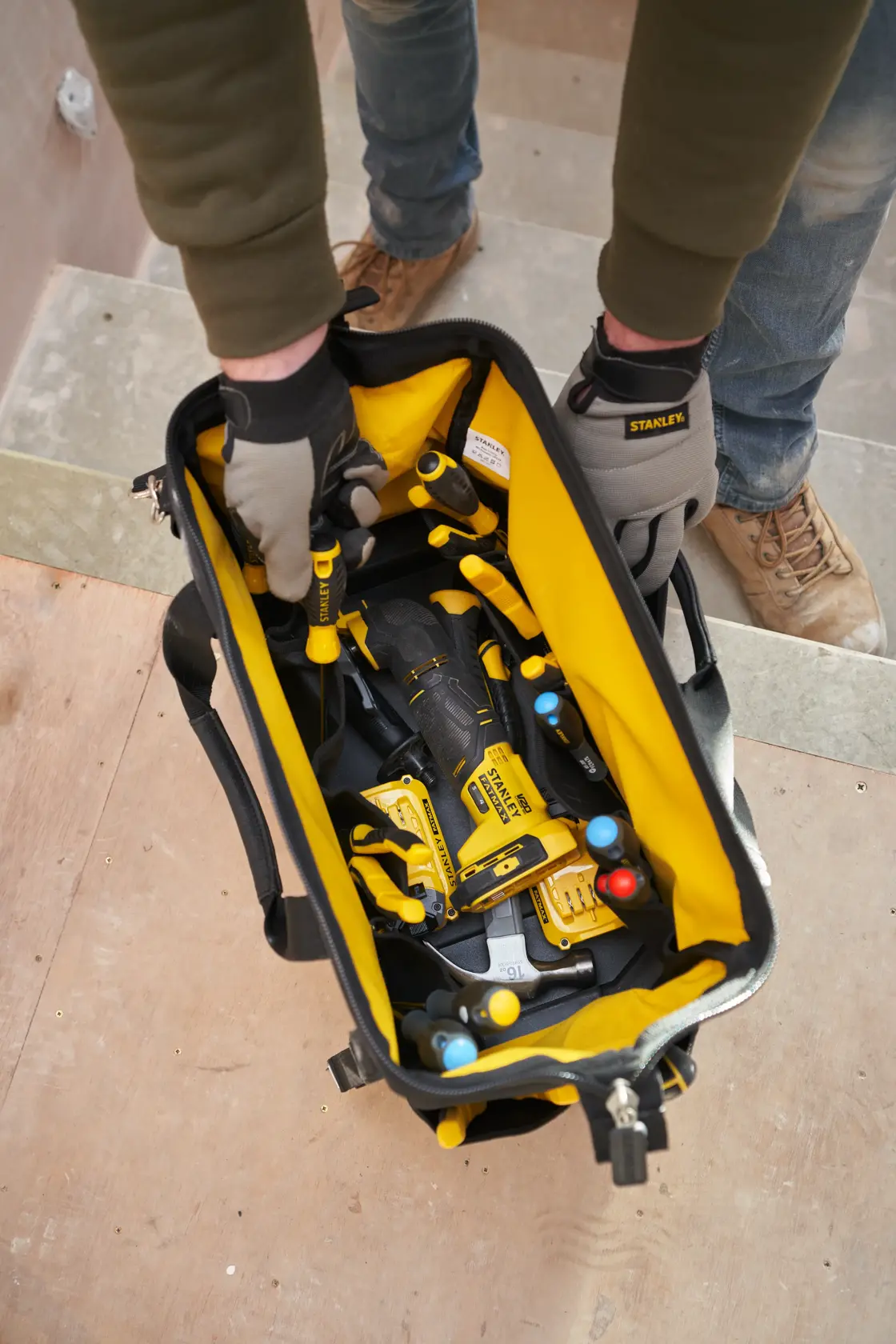 STANLEY FMST17627-1 tool bag with yellow interior filled with hand tools, shown from above on a worksite.