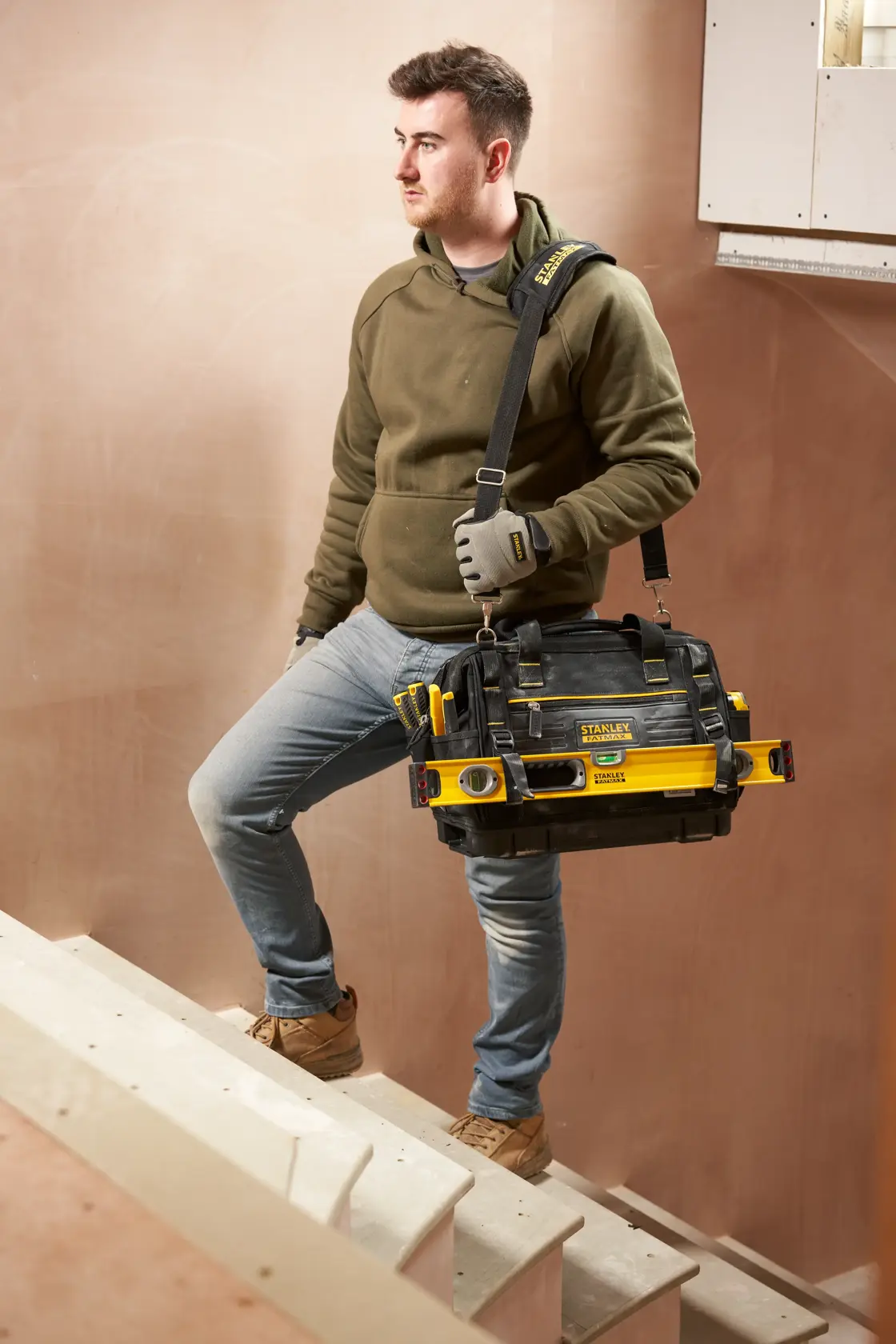 STANLEY FMST17627-1 tool bag with shoulder strap and attached tools, carried by person on stairs.