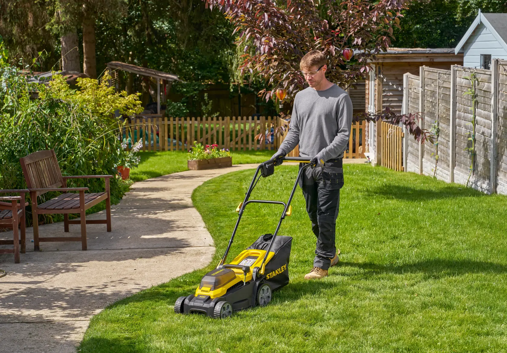 STANLEY SCMWP3401M1-XE lawn mower in use on grass in a garden setting, side angle.