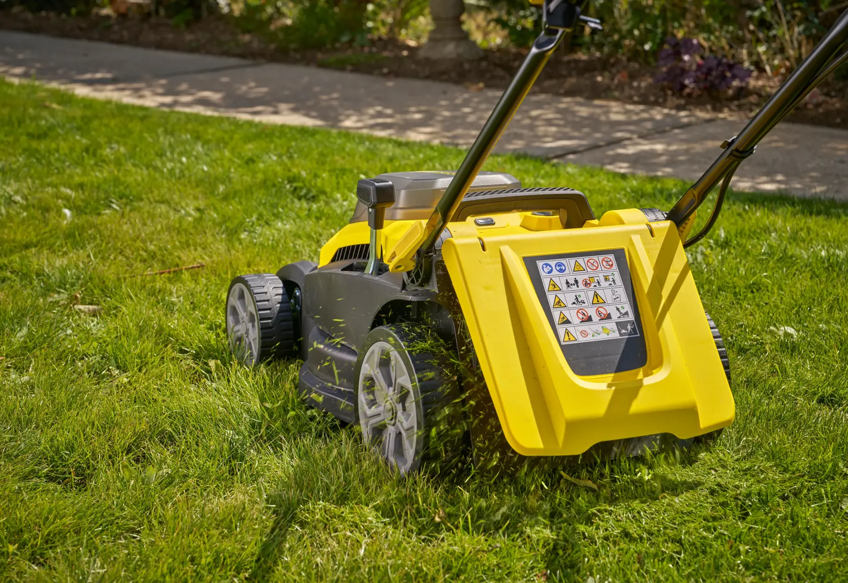 STANLEY SCMWP3701N lawn mower side view on grass, yellow body, warning label visible, large rear wheels.