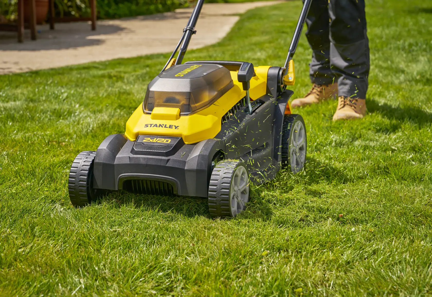 STANLEY SCMWP3701N lawn mower in yellow and black, shown in use on grass, with visible cuttings and user’s legs.