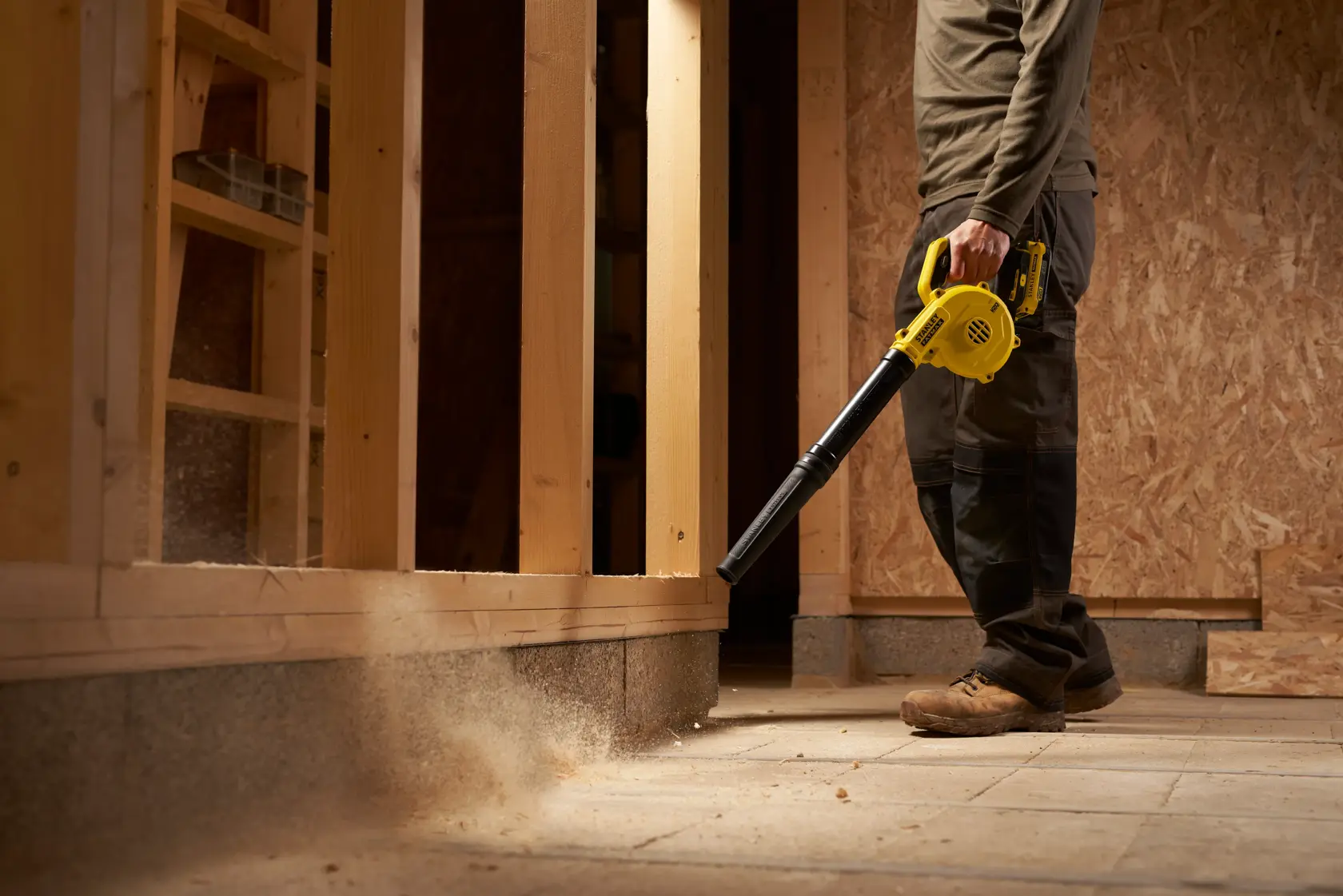 STANLEY SFMCBL01B blower in use on construction site, yellow cordless tool clearing dust from floor.