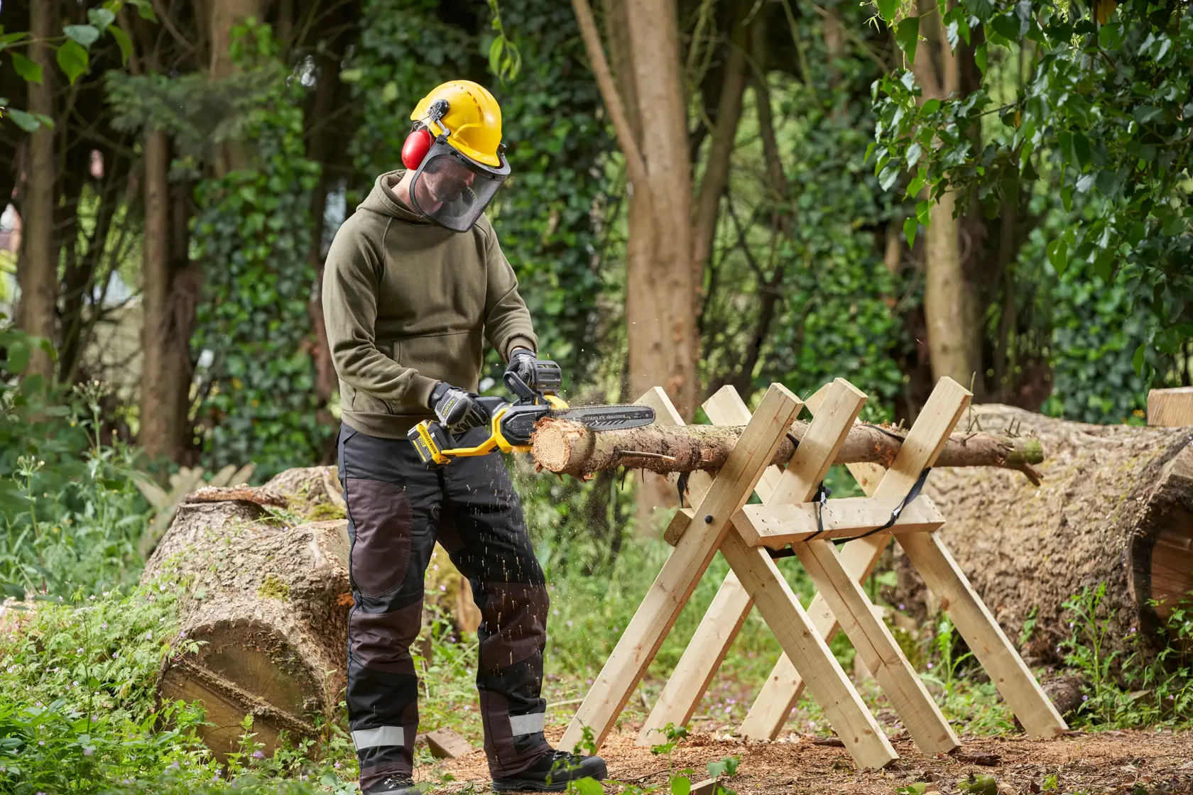 STANLEY SFMCCS730B chainsaw cutting log outdoors with user wearing safety gear, product in use in wooded area.