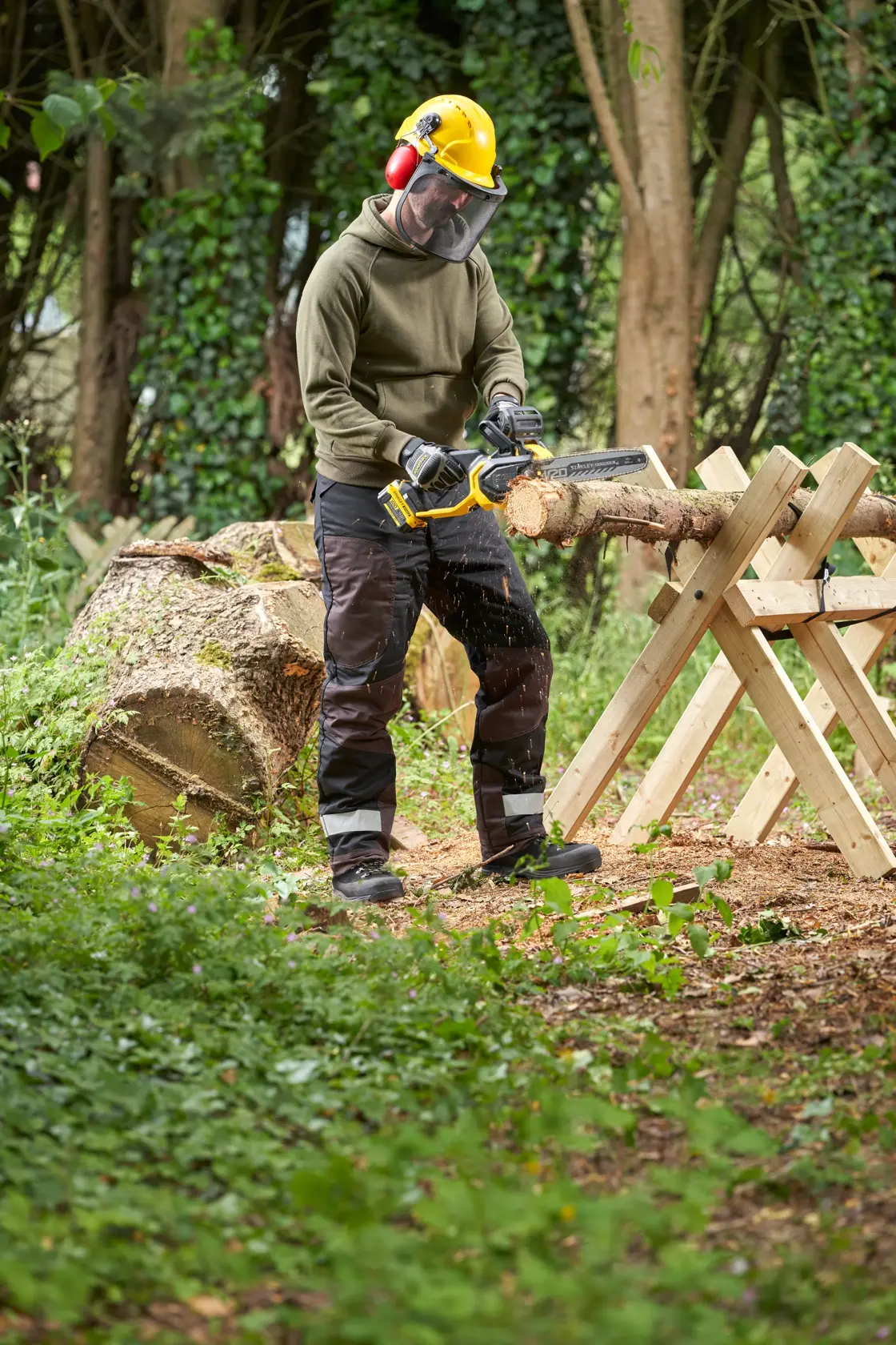 STANLEY SFMCCS730B chainsaw in use cutting wood outdoors, operator wearing safety gear, forestry setting.