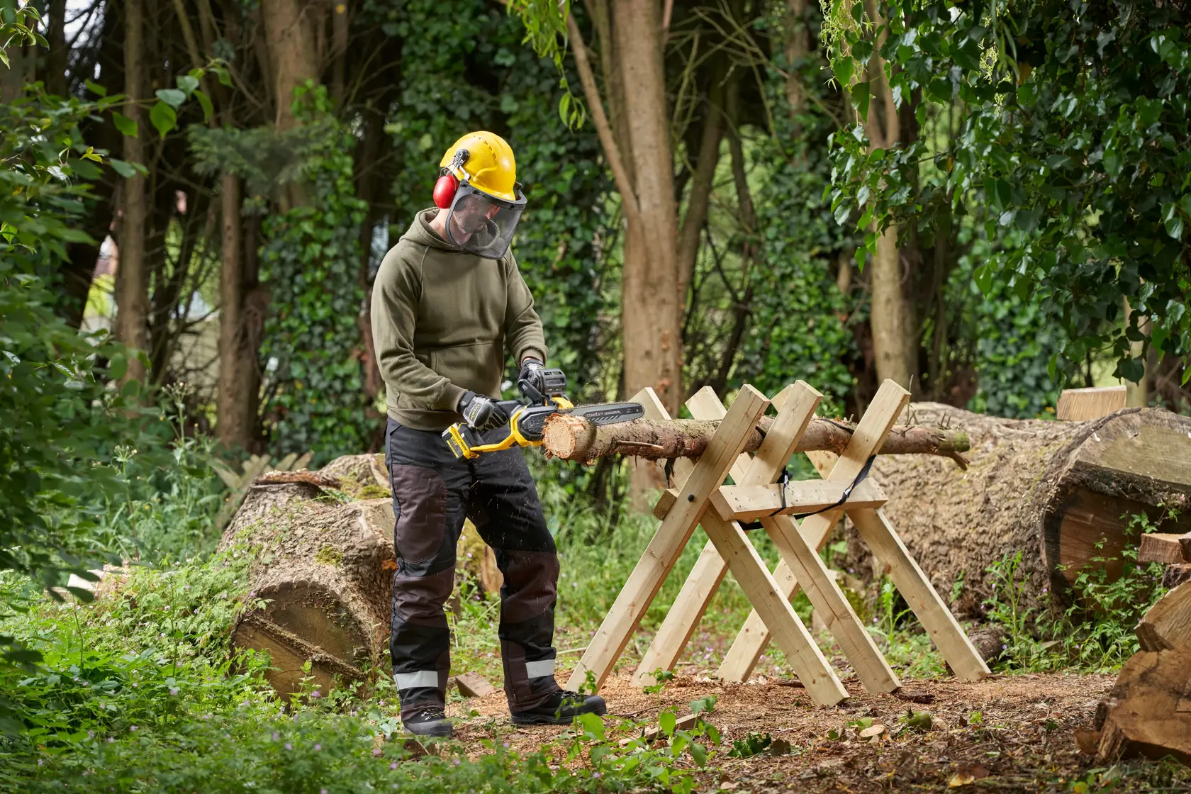 STANLEY SFMCCS730M1 cordless chainsaw in use outdoors cutting a log on a wooden sawhorse.