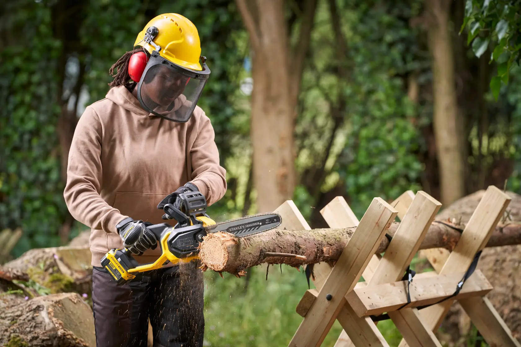 STANLEY SFMCCS730M1 cordless chainsaw in use cutting a log outdoors, person wearing safety gear.
