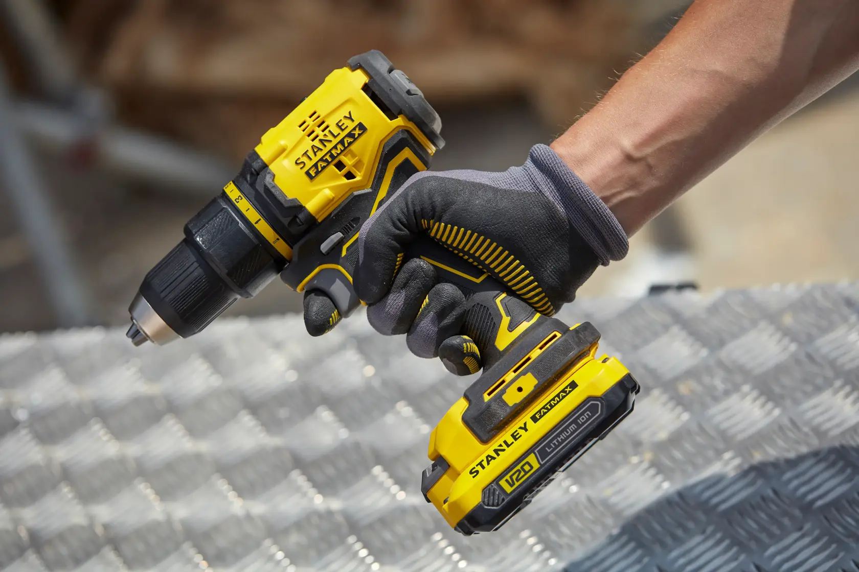 Photo of STANLEY SFMCD710C2K cordless drill in yellow and black, held by a gloved hand on metal surface.