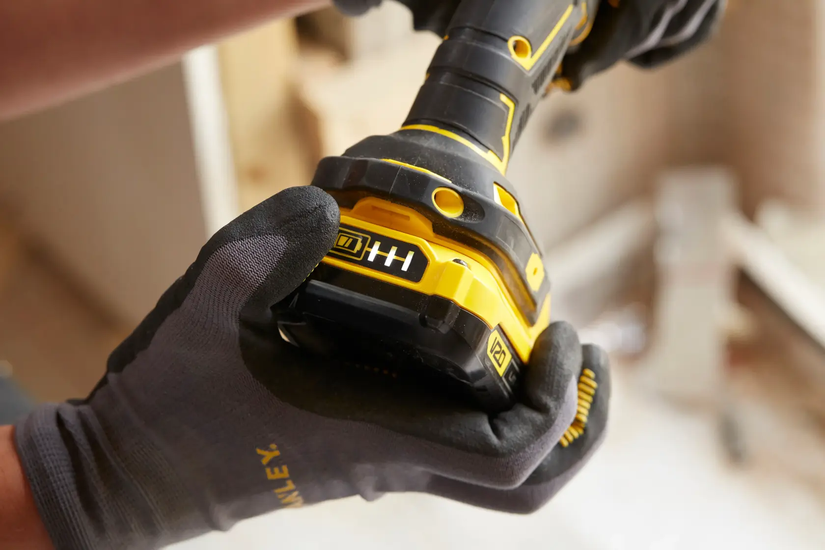 STANLEY SFMCD710C2K cordless drill held by gloved hand, close-up view showing yellow and black design.