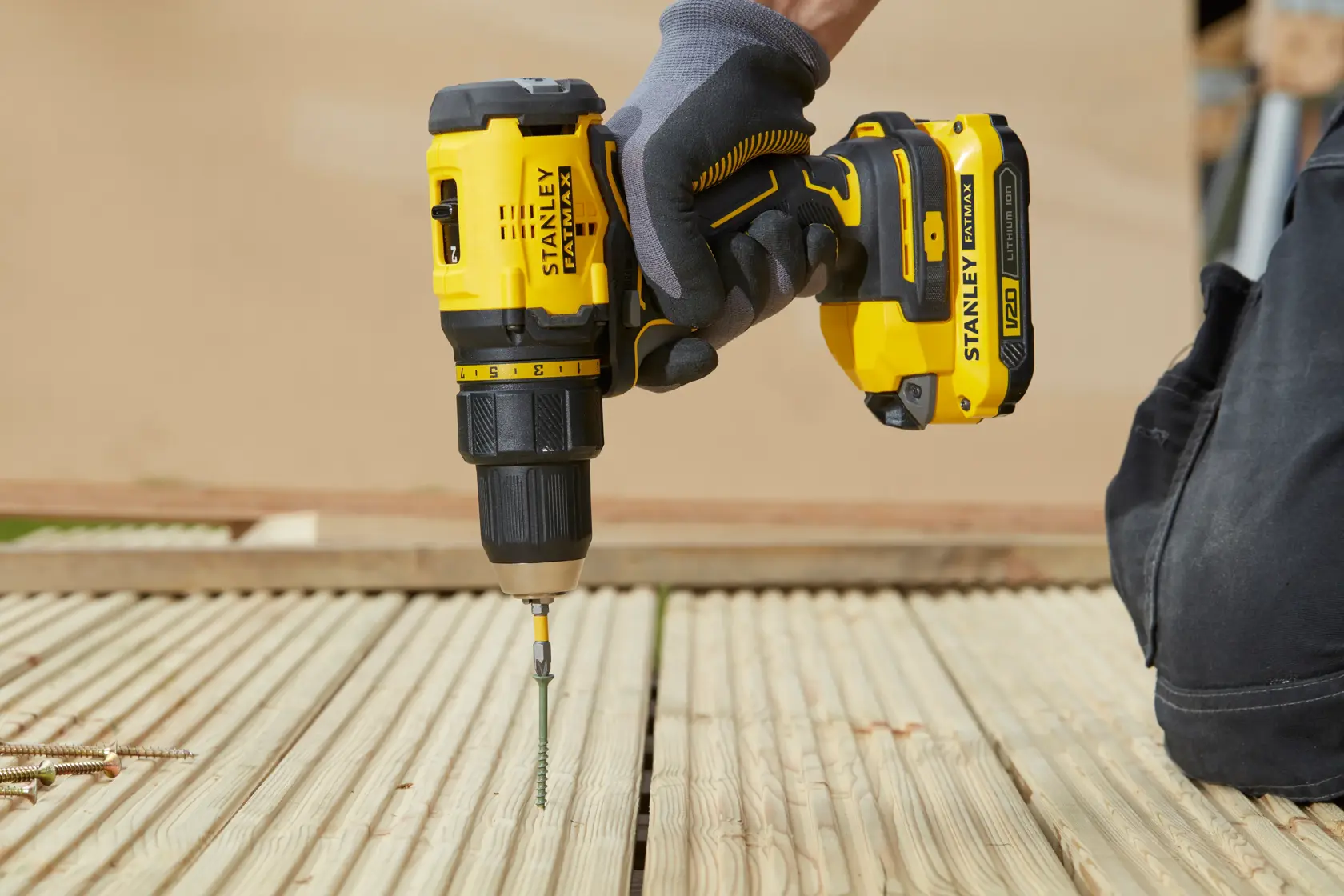 Stanley cordless drill driving a screw into wooden decking. Gloved hand holding the tool.