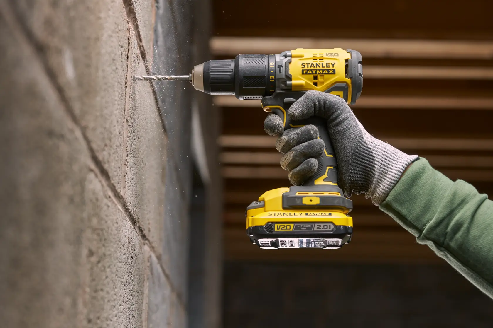 STANLEY SFMCD715D1K cordless drill in use, drilling into a concrete wall, side view, yellow and black design.