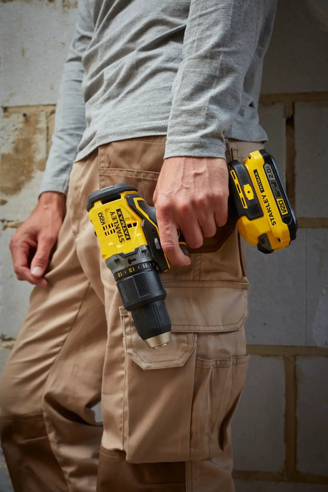 Photo of worker holding STANLEY SFMCD715D2K cordless drill, yellow and black, by side, close-up view.