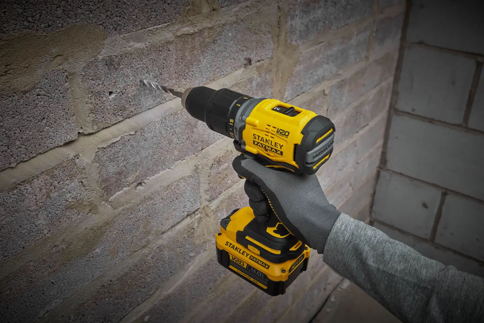 STANLEY SFMCD715M2K cordless drill in use drilling into a brick wall, bright yellow and black design.