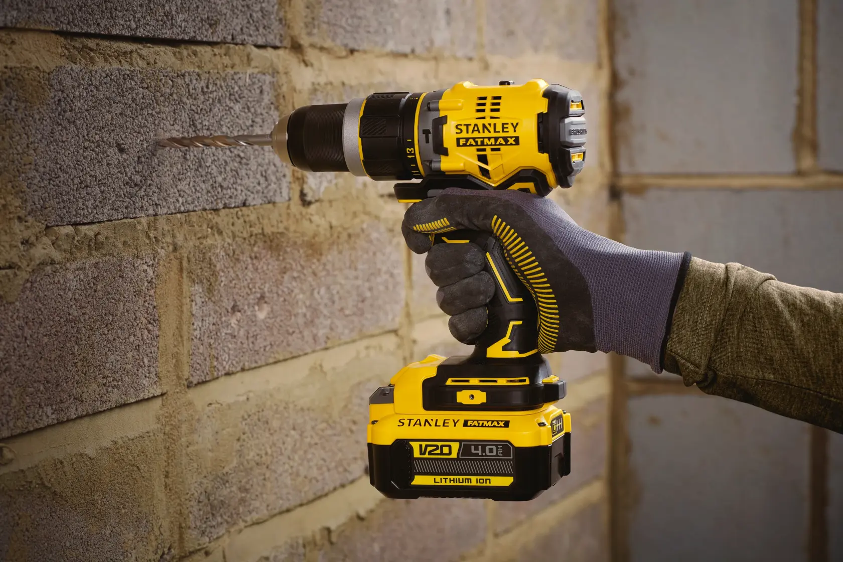 STANLEY SFMCD721M2K cordless drill in use, drilling into brick wall, yellow and black design, Photography product.