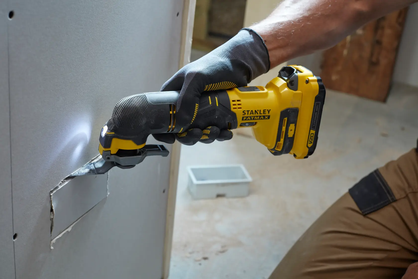 STANLEY SFMCE500B oszillierendes Multitool schneidet Trockenbauwand, Arbeiter mit Handschuhen, gelb-schwarzes Design.