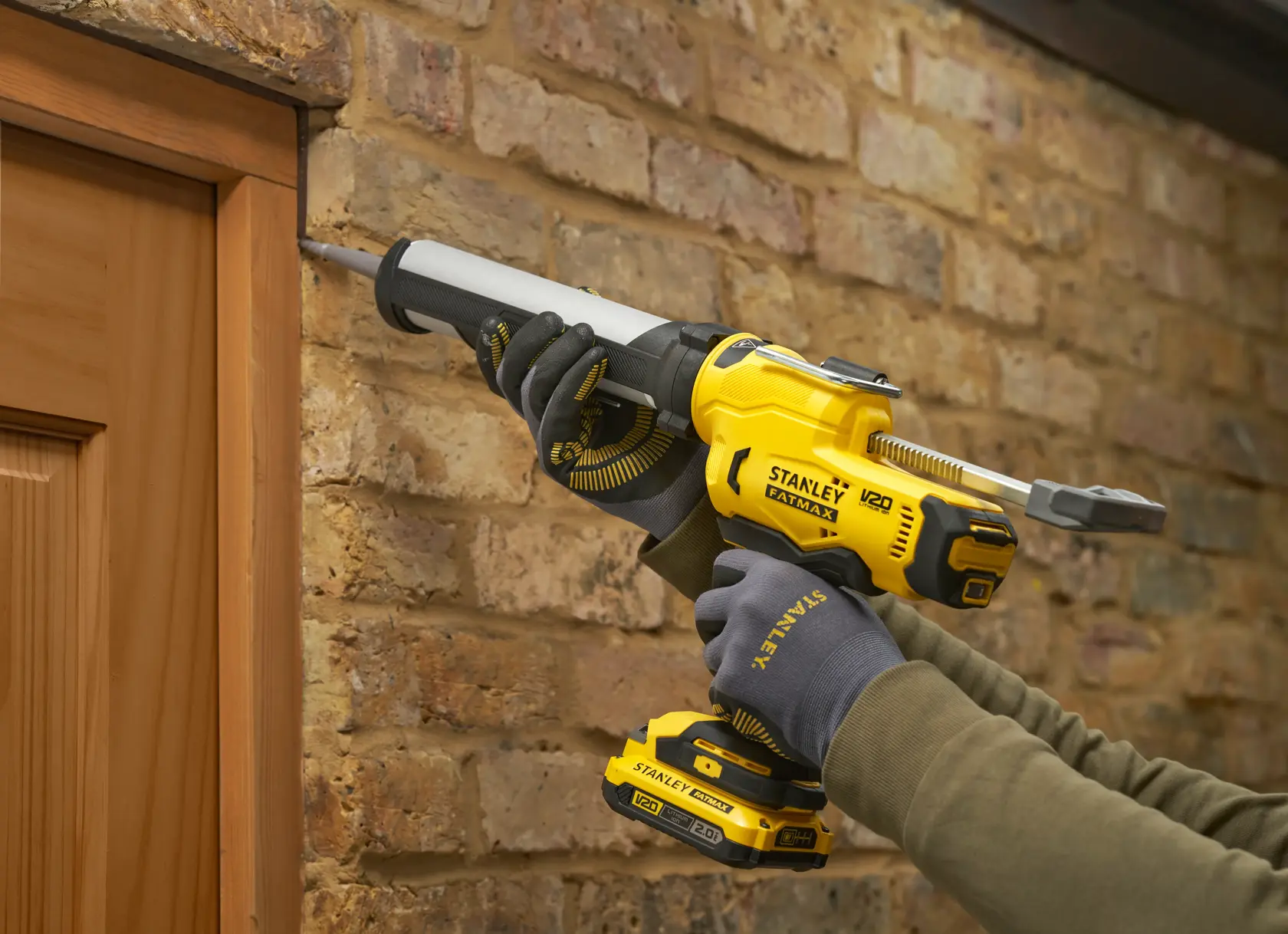 STANLEY SFMCE600B caulk gun used to seal around a wooden door frame against a brick wall.