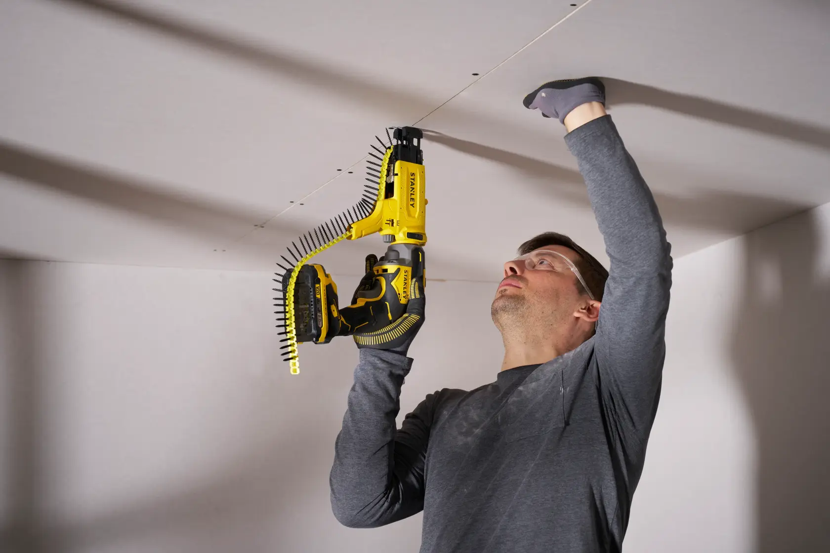 STANLEY SFMCF600B drywall screw gun in use for ceiling installation, front angle, yellow and black tool.