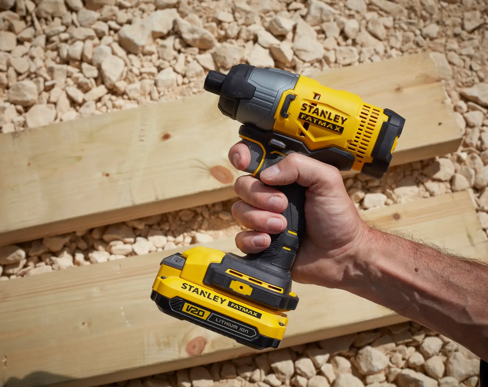 Photo of a STANLEY SFMCF800C2K cordless impact driver held in hand, yellow and black, outdoors on wood boards.