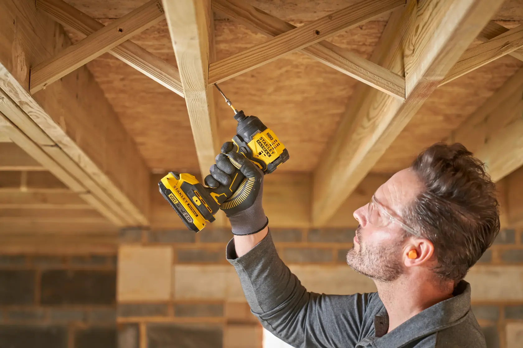 STANLEY SFMCF811D1T cordless impact driver used to drill into wooden beams in a construction setting.