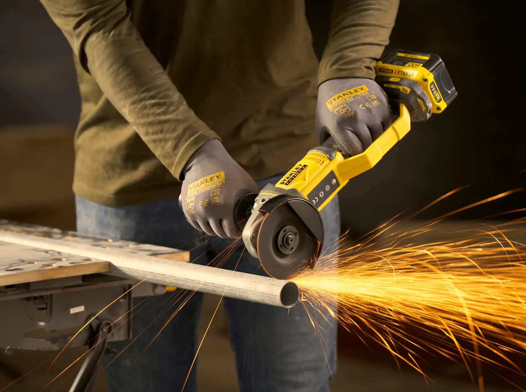 Photo of STANLEY SFMCG300B cordless angle grinder in use cutting metal pipe, producing bright sparks.