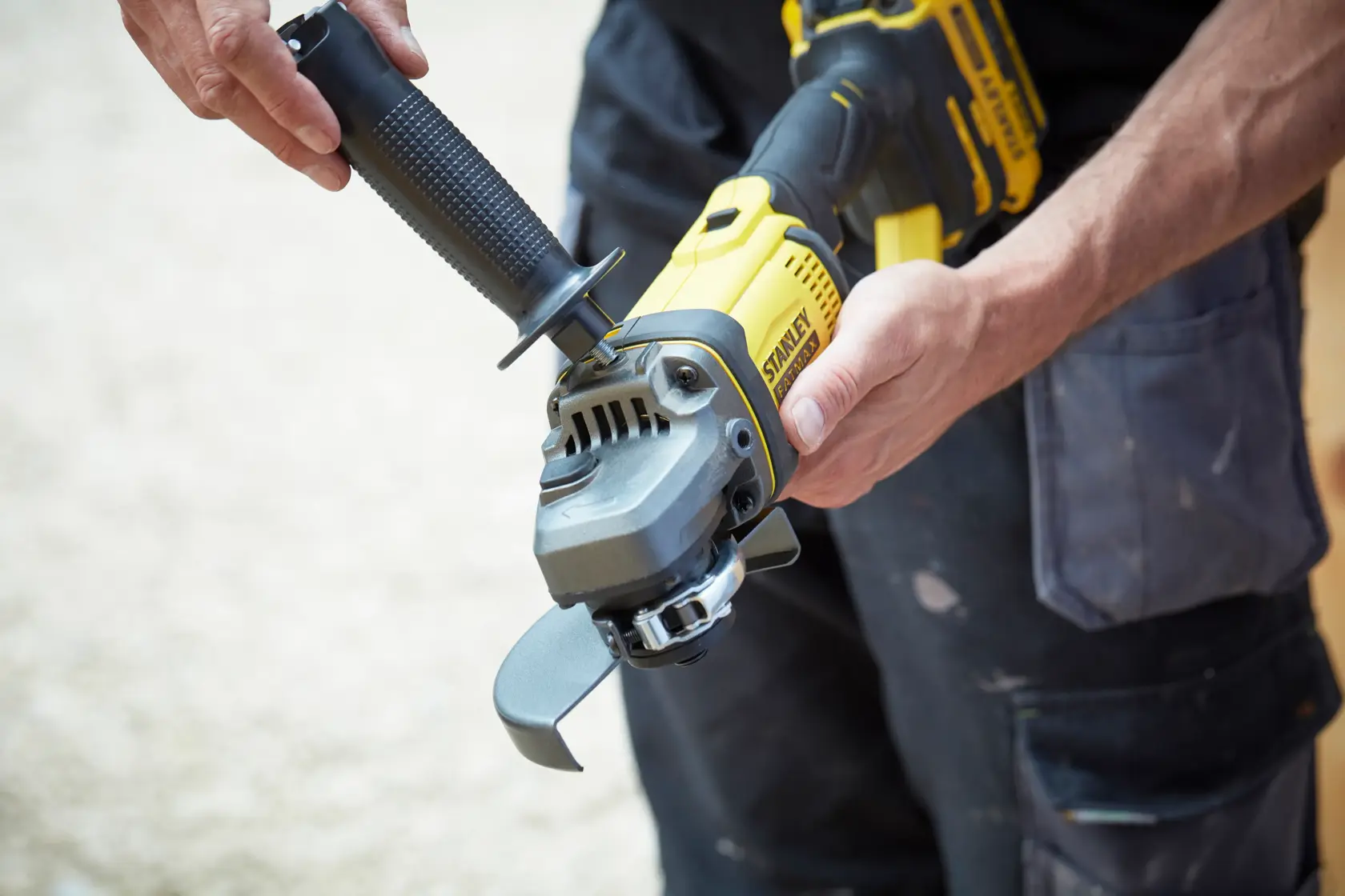Photo of STANLEY SFMCG400B cordless angle grinder being held and assembled by a person in workwear.