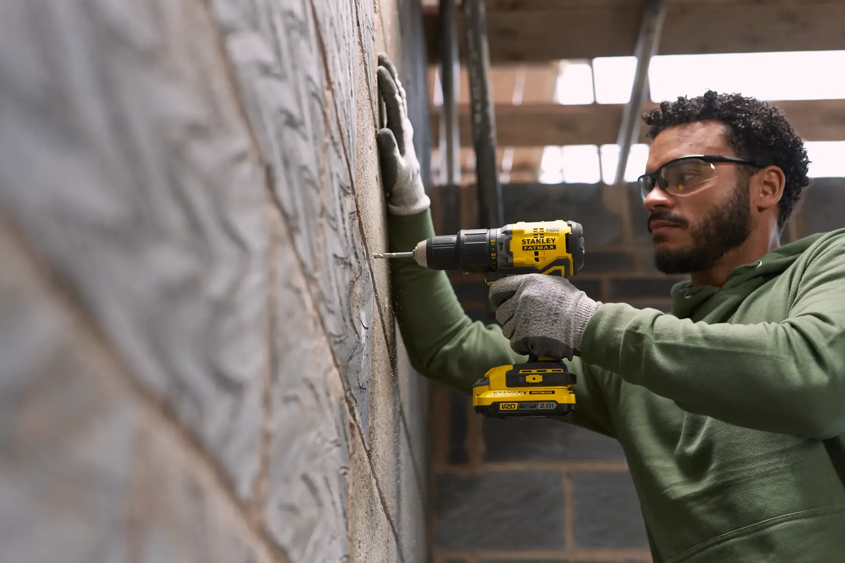 Photo of STANLEY SFMCK461D2T cordless drill in use drilling into a block wall, construction setting.