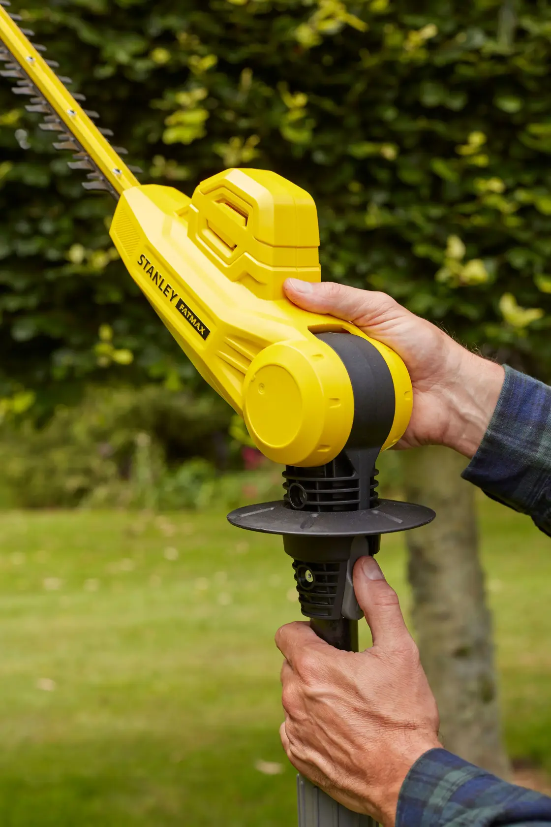 Photo of STANLEY SFMCPH845B hedge trimmer held in hands, showing yellow body and blade outdoors.