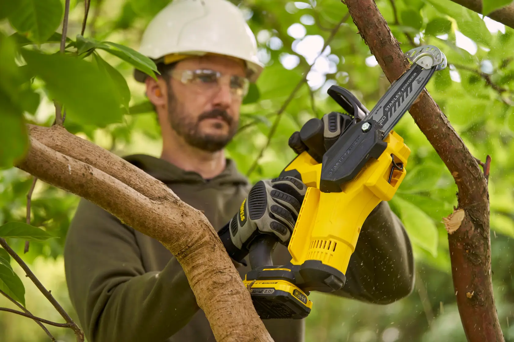 Photo of STANLEY SFMCPS415B cordless chainsaw in use, yellow and black, cutting tree branch outdoors.