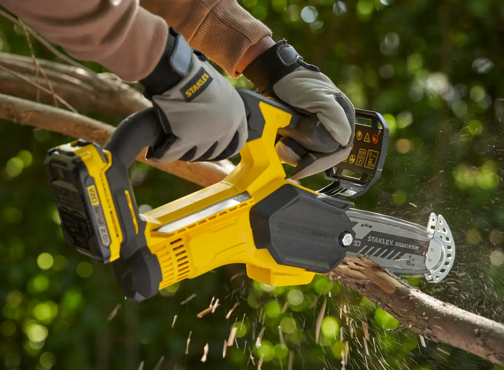 Photo of STANLEY SFMCPS415B cordless pruning saw cutting a tree branch, user wearing gloves outdoors.