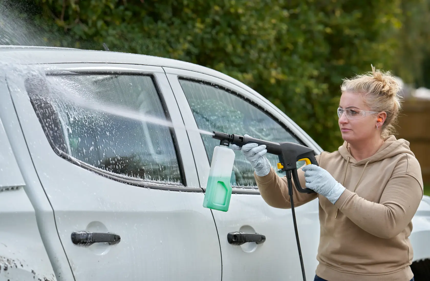 STANLEY SFMCPW1500B pressure washer in use cleaning a white car, side view, outdoors.
