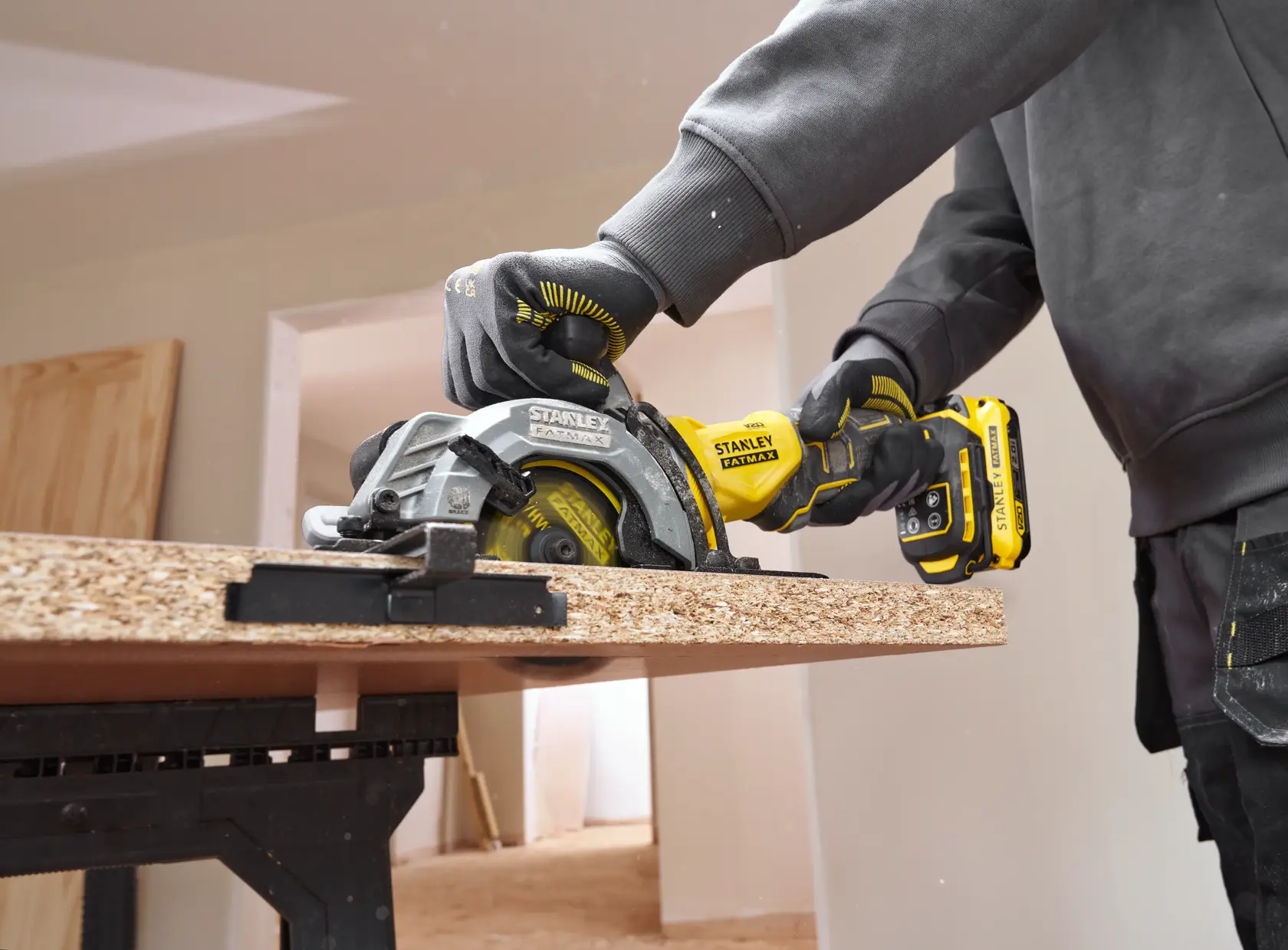 Stanley SFMCS515B cordless circular saw, side angle, cutting wood panel indoors.