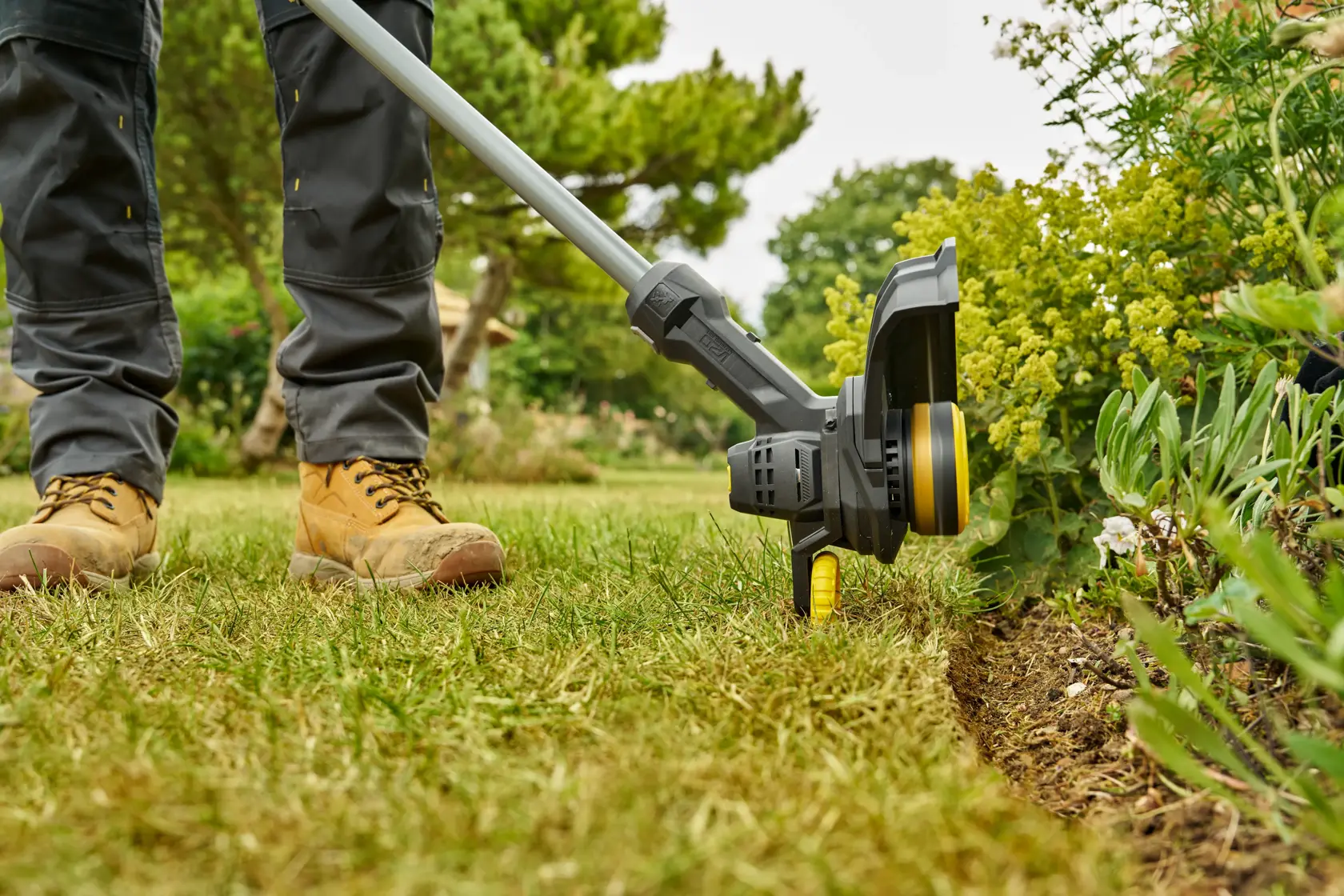 Photo of STANLEY SFMCST925B string trimmer in use edging a garden lawn, close-up, outdoors.