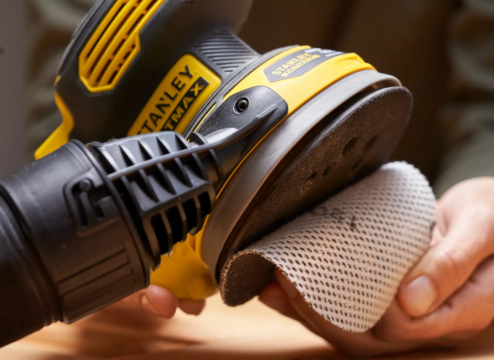 STANLEY SFMCW220B sander held in hand, mesh sanding pad being attached, close-up view.