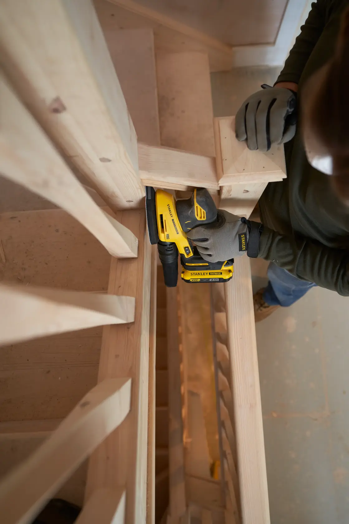 STANLEY SFMCW221D1S cordless sander used on wooden staircase, close-up of tool in action.