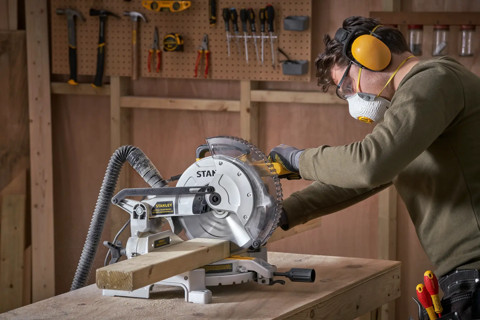 Photo of STANLEY SM1650 miter saw cutting wood in workshop with person wearing safety gear.