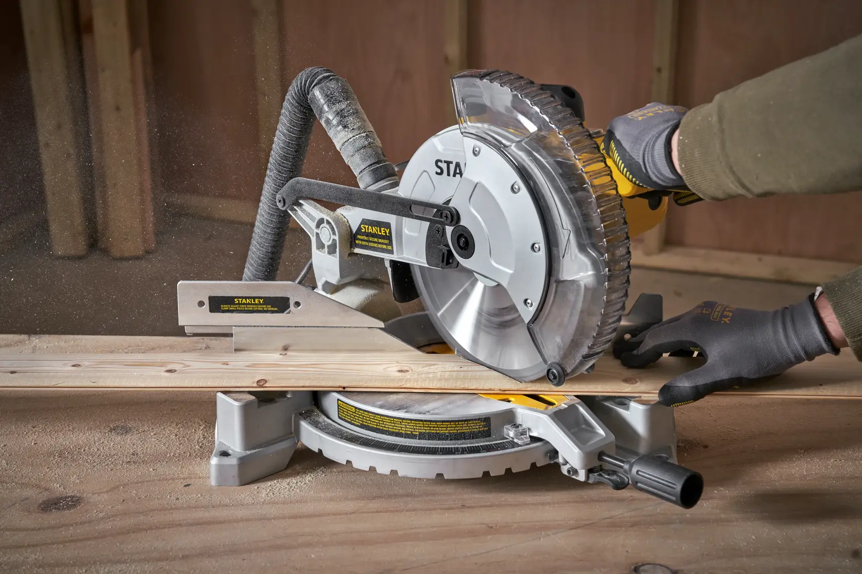 STANLEY SM1650 miter saw cutting wood, close-up side angle, worker wearing gloves in workshop.