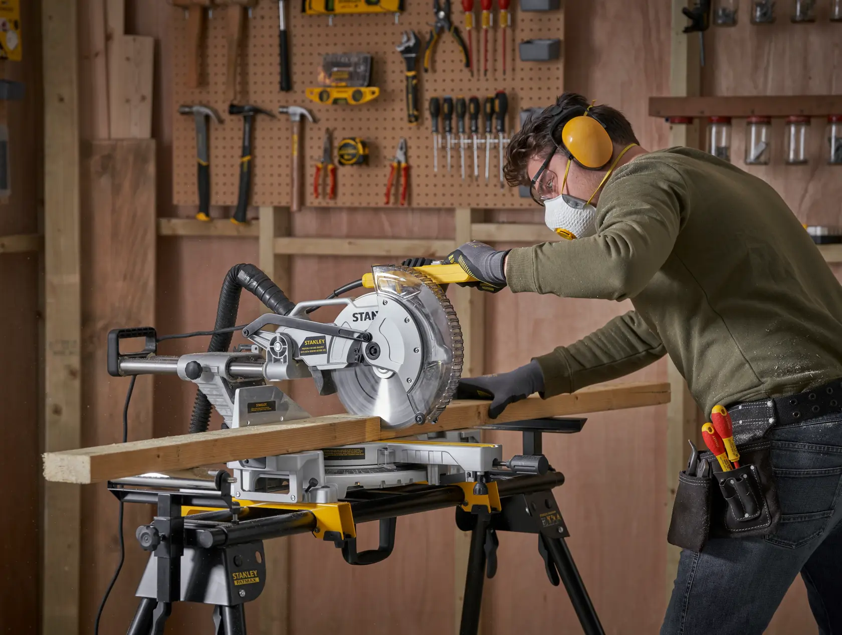 STANLEY SM1800 miter saw in use, cutting wood in workshop with tools on wall, side view.