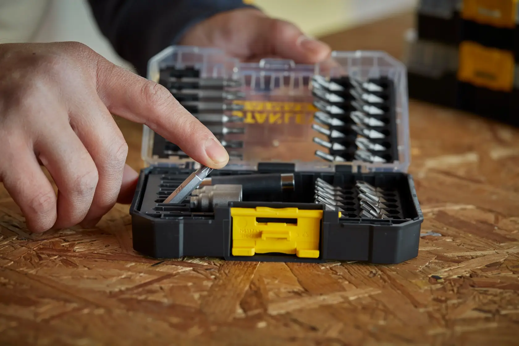 STANLEY STA88560 drill bit set case with yellow latch, person selects a bit, close-up on wooden surface.