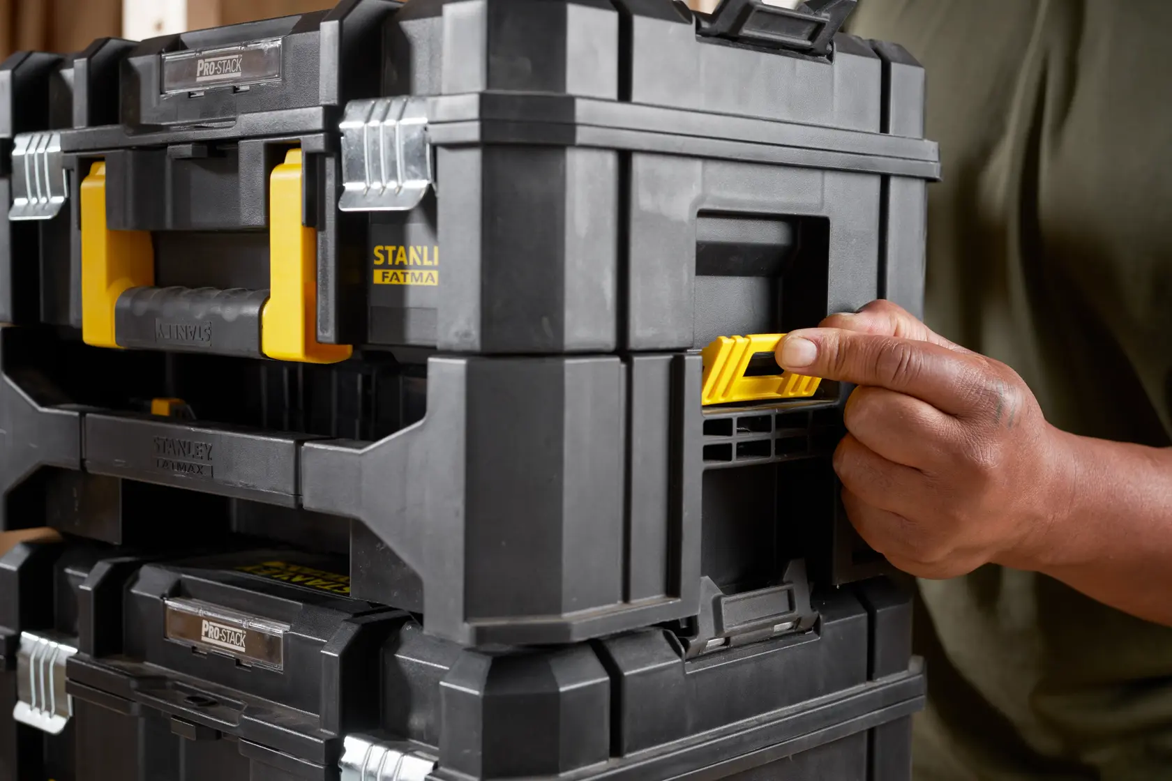 STANLEY STA88580 black and yellow PROSTACK toolbox, close-up side angle, hand pressing yellow latch.
