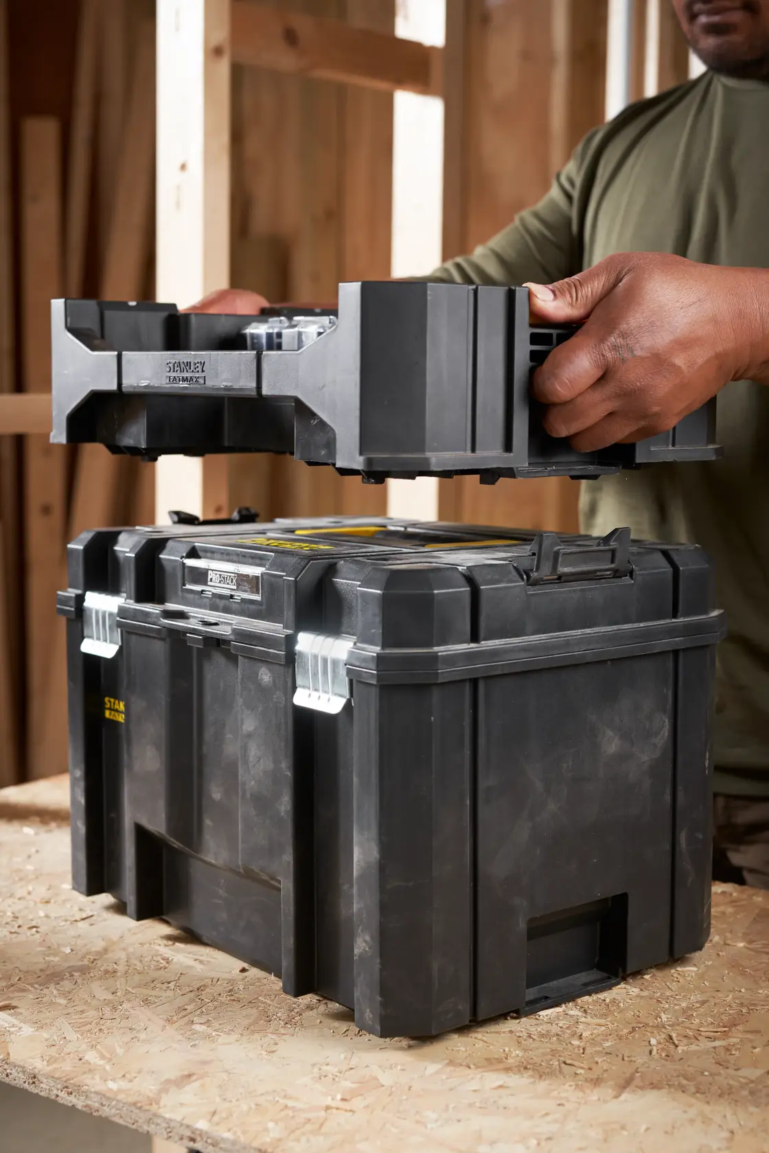STANLEY STA88580 black stackable tool box with metal latches, shown in workshop, person stacking trays.