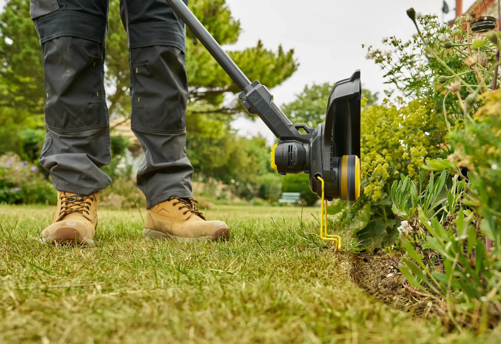 STANLEY STCST933B grass trimmer in use on lawn edge, close-up side view, showing trimming near flower bed.