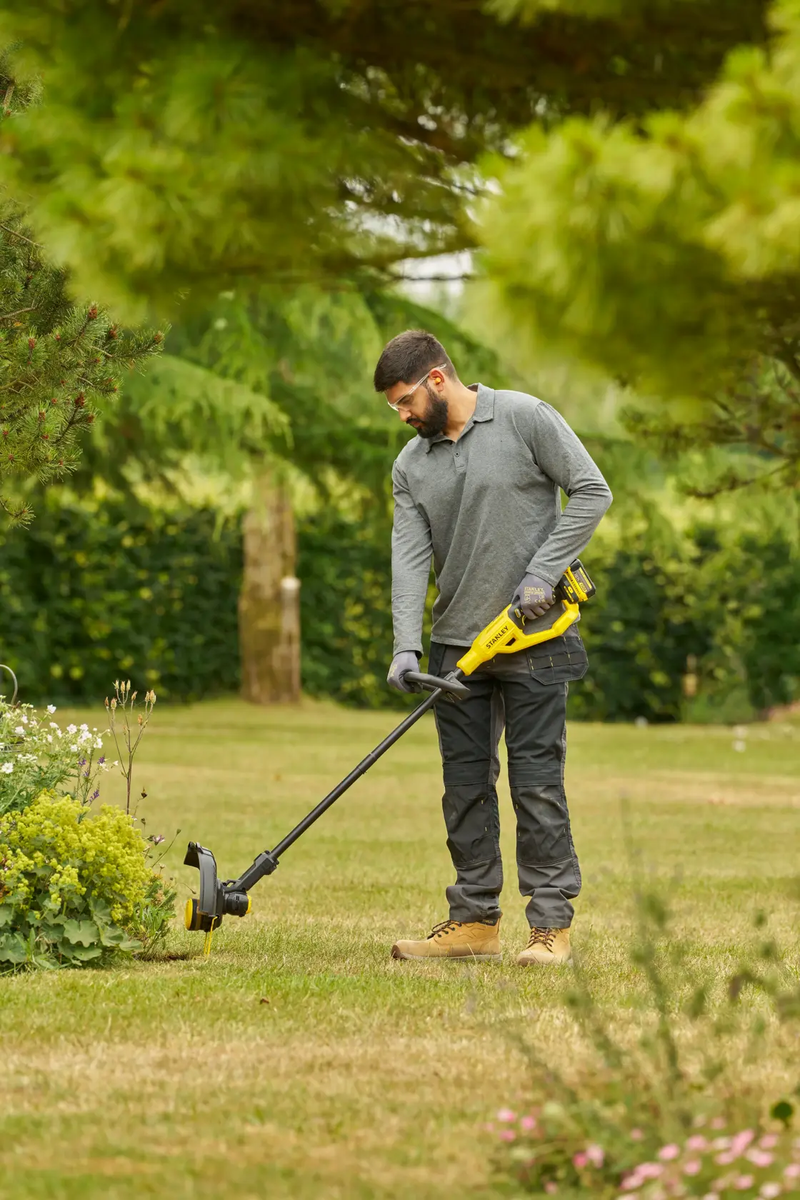 STANLEY STCST933M1 grass trimmer used outdoors in garden, yellow and black design, battery powered.