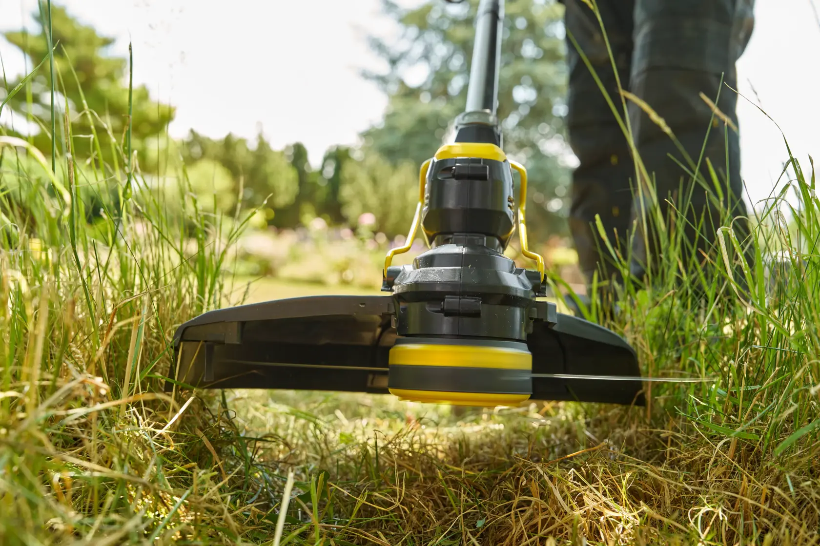 STANLEY STCST933M1 grass trimmer close-up, in use on lawn with green grass, photographed outdoors.