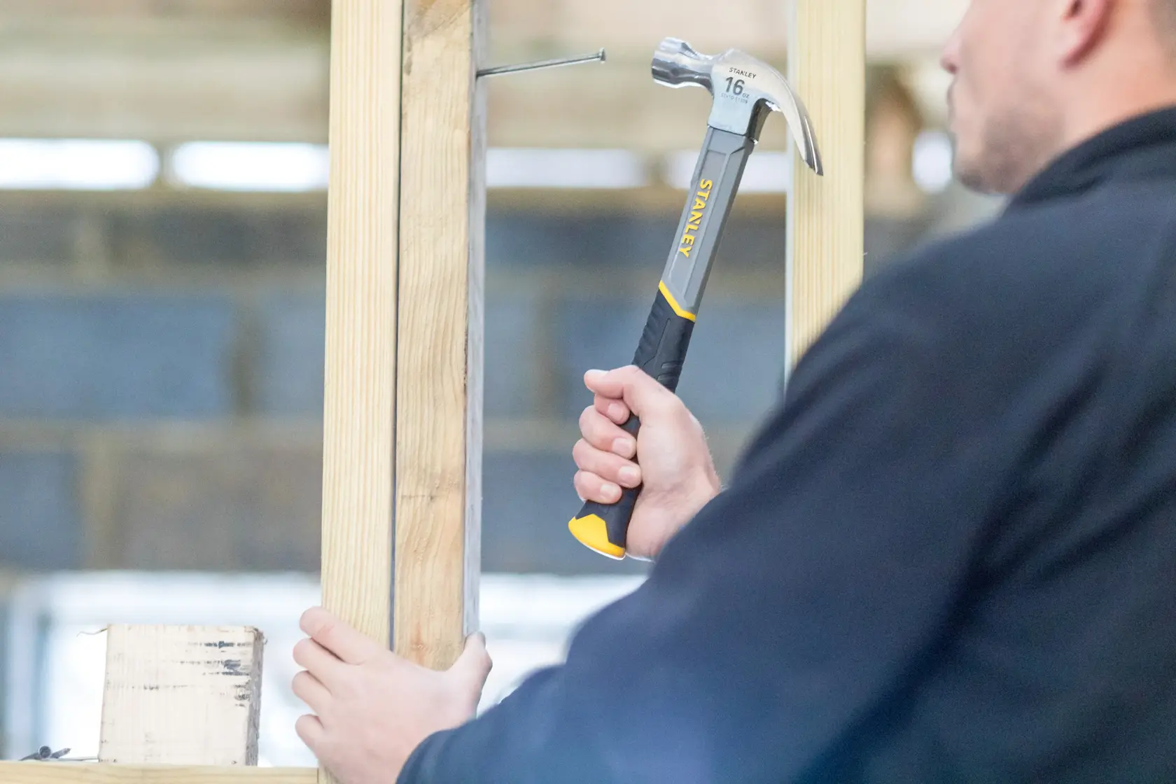 Person using STANLEY STHT0-51310 claw hammer on wood frame, close-up photo of tool handle and head.