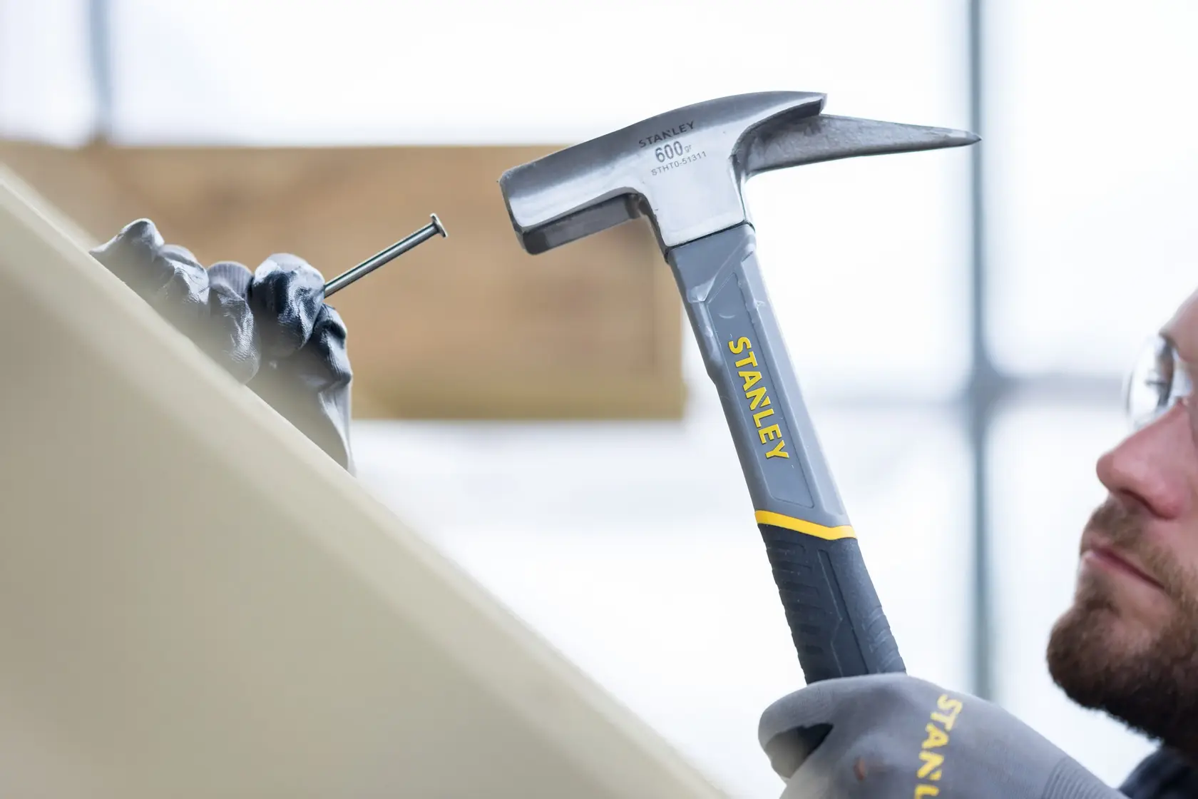 STANLEY STHT0-51311 hammer in use, striking a nail held by a gloved hand, close-up view.