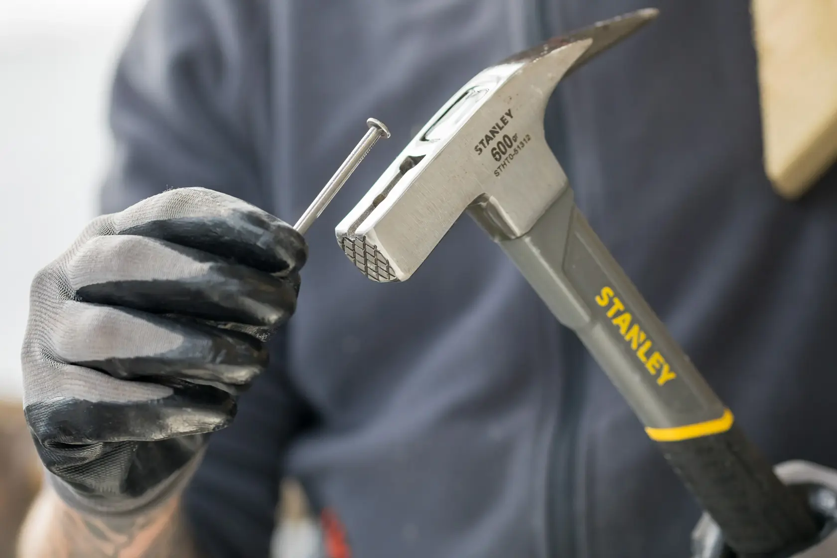 Stanley STHT0-51312 hammer held with gloved hand, positioning a nail, close-up photo.